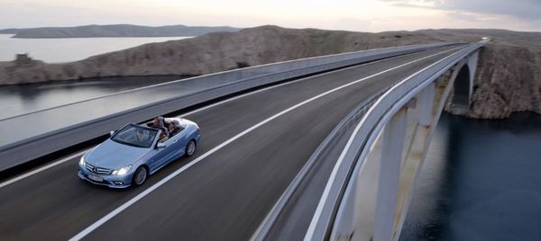 2011 Mercedes-Benz E350 Cabriolet in motion on a scenic road, showcasing its elegant design and open-top experience.