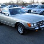 Front three quarter view of a red 1985 Mercedes-Benz 380SL parked outdoors.