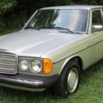 Front view of a faded red 1980 Mercedes-Benz 300D with fog lights illuminated, showcasing its classic design.